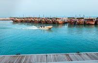 A serene view of traditional wooden dhows docked at a Middle Eastern port with a motorboat passing by.