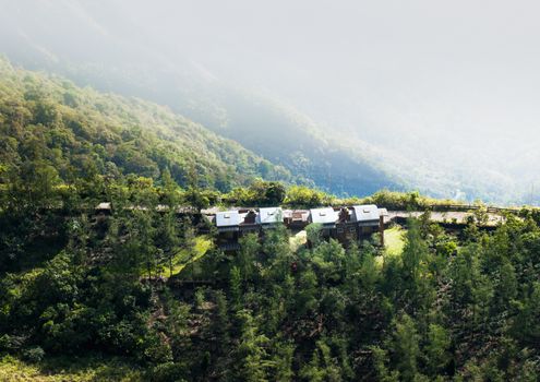 Aerial view of picturesque lodges nestled in a foggy, lush green mountain valley, creating a serene retreat.