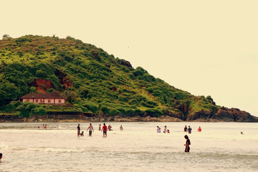 People enjoying a sunny day at a scenic beach with lush green hillside in Karnataka, India.