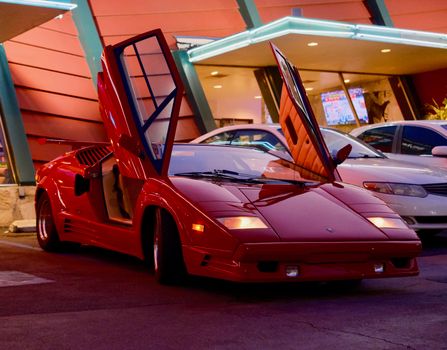 A classic red sports car with open doors parked in West Hollywood at night, showcasing retro style and elegance.