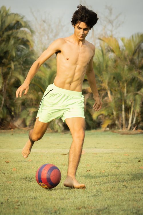 Free A young man plays barefoot football on a grassy field surrounded by palm trees, captured in natural lighting. Stock Photo