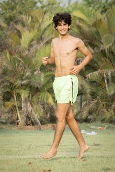 A smiling young man jogging outdoors in a grassy area, embracing fitness and wellness.
