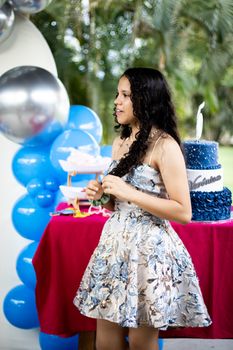 Teen girl celebrates birthday outdoors with blue-themed decorations and cake.