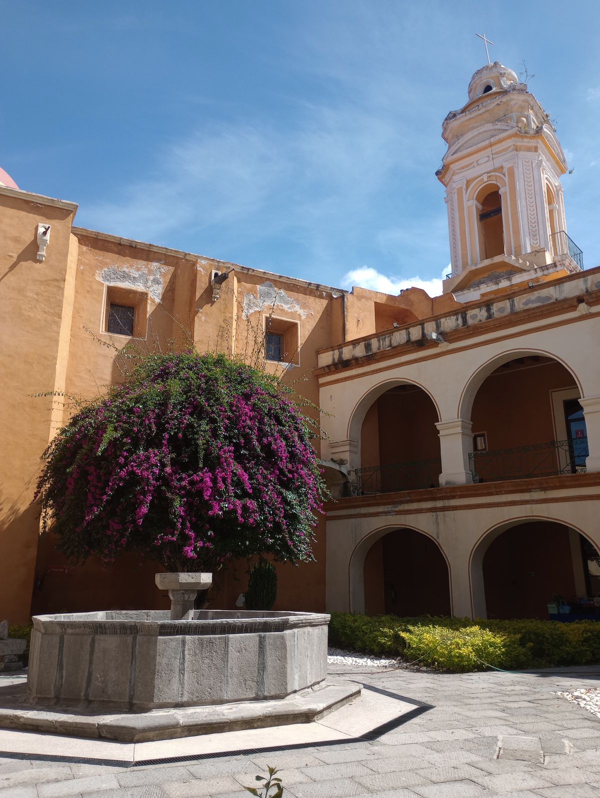 Colonial courtyard with a stone fountain, arches and purple bougainvillea