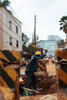 Construction worker with hard hat using a pickaxe in an urban street setting, symbolizing infrastructure development.
