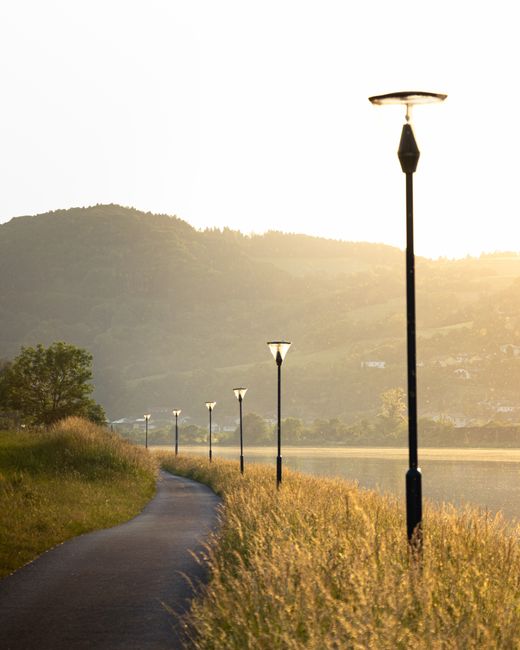 Serene lakeside pathway illuminated by lamp posts under a golden sunset, offering tranquility and beauty.