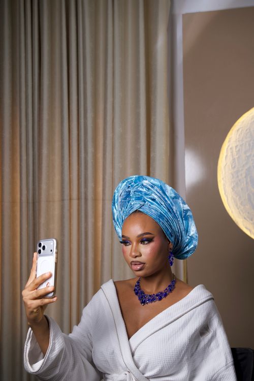 Free A stylish woman in a blue gele headwrap and robe taking a selfie indoors. Stock Photo