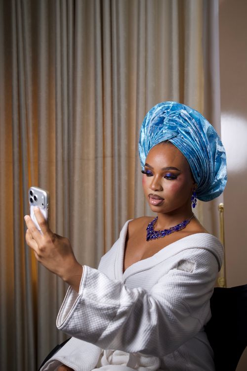 Free A sophisticated portrait of a woman in a blue gele and robe capturing a selfie indoors. Stock Photo