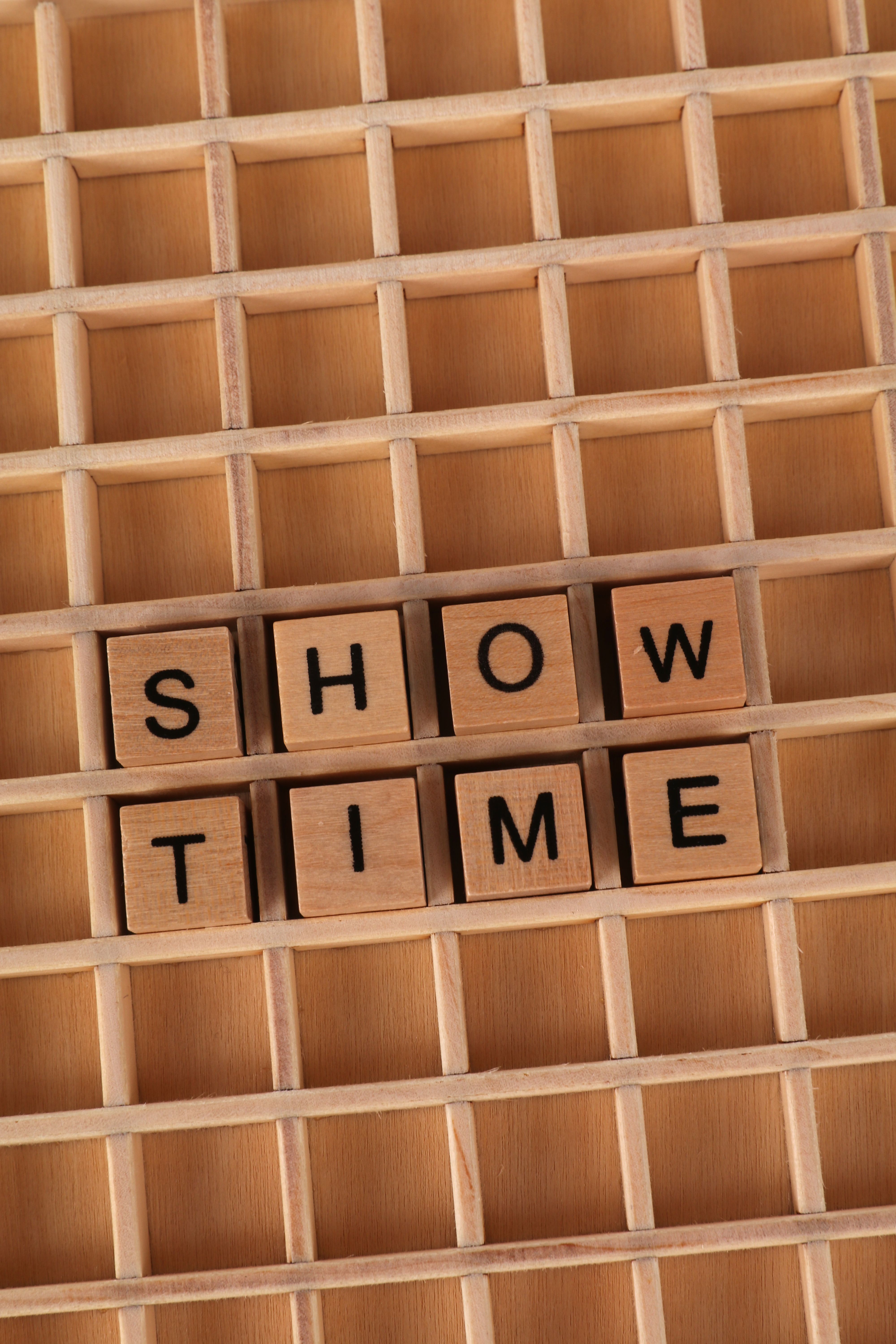 Wooden letter tiles arranged to spell 'Showtime' on a wooden grid background.