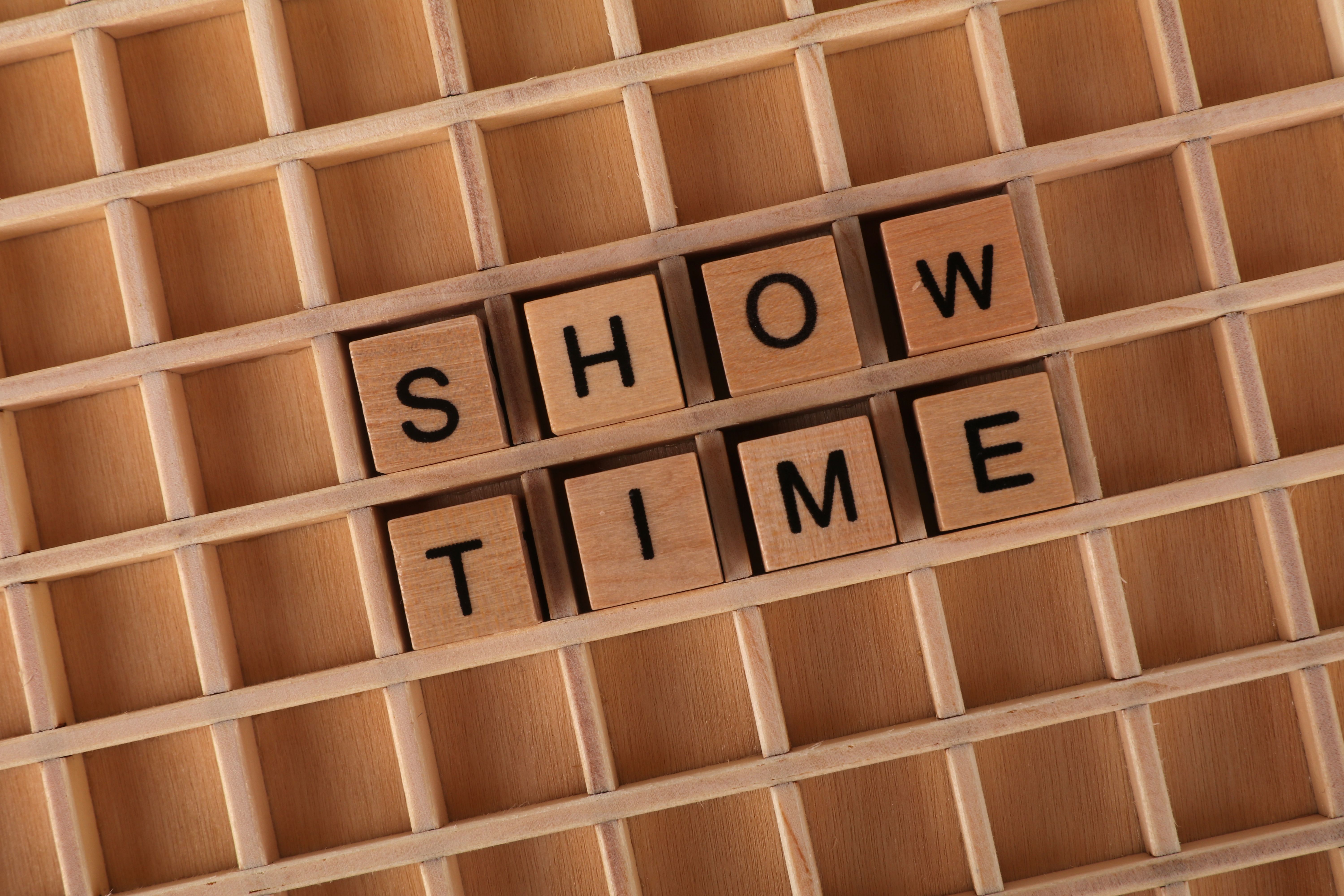 Wooden letter blocks arranged to spell 'Show Time' on a wooden grid background.