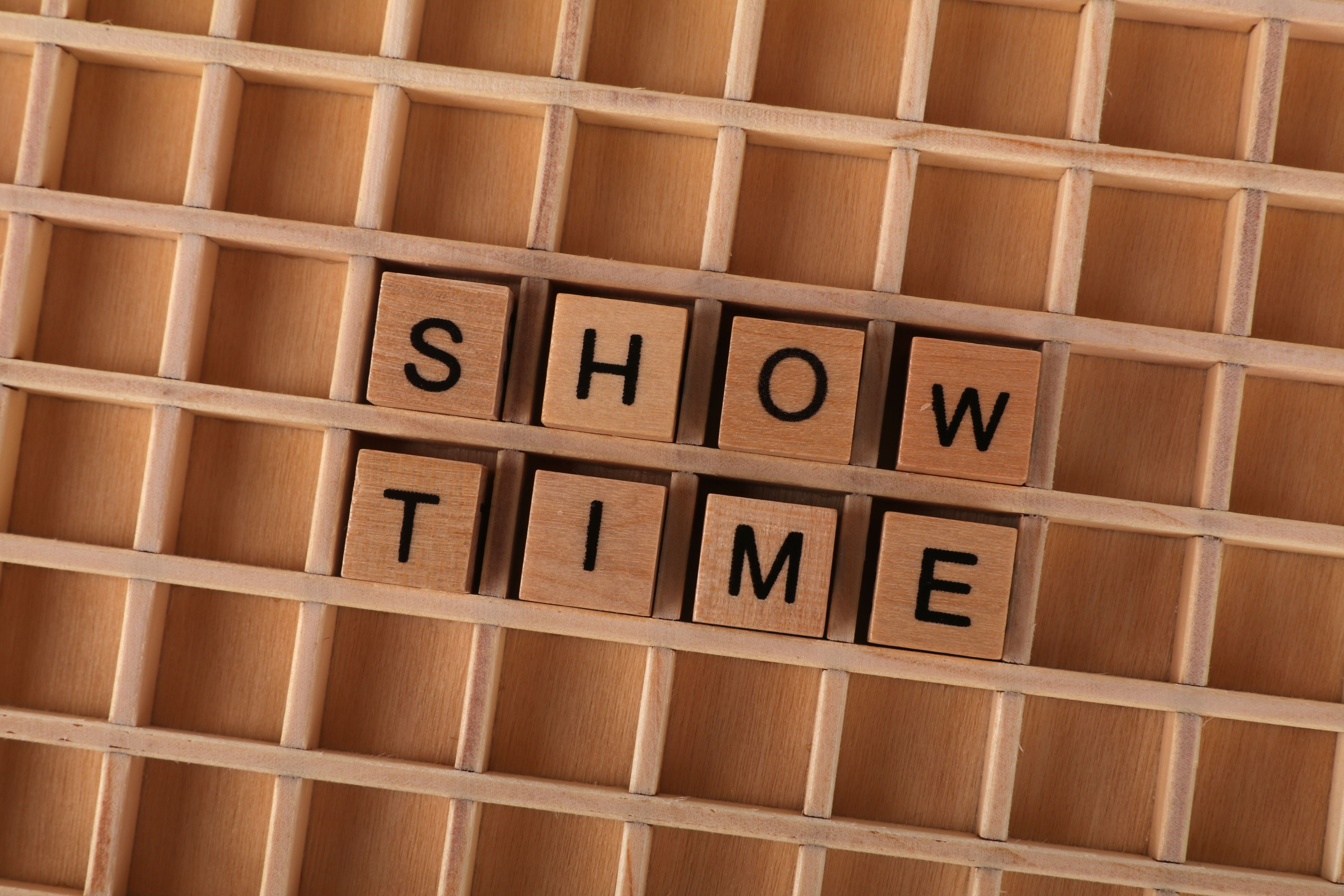 Wooden letter tiles arranged to form the words SHOW TIME on a wooden grid background.