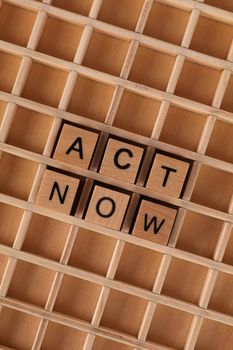 Wooden blocks spelling 'ACT NOW' on a wooden grid background, emphasizing urgency.
