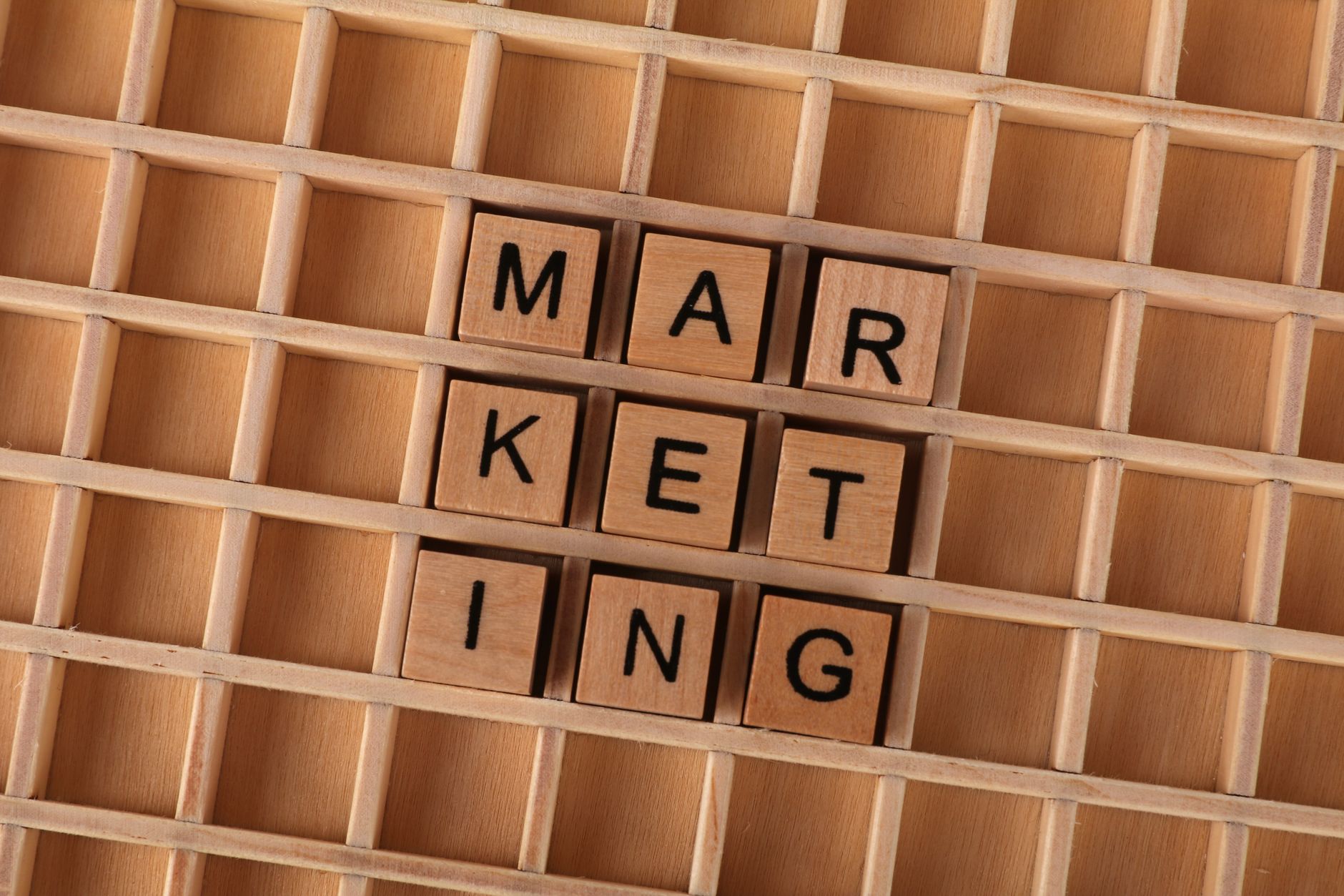 Wooden letter tiles spell out the word marketing on a grid background, showcasing creativity and business concept.