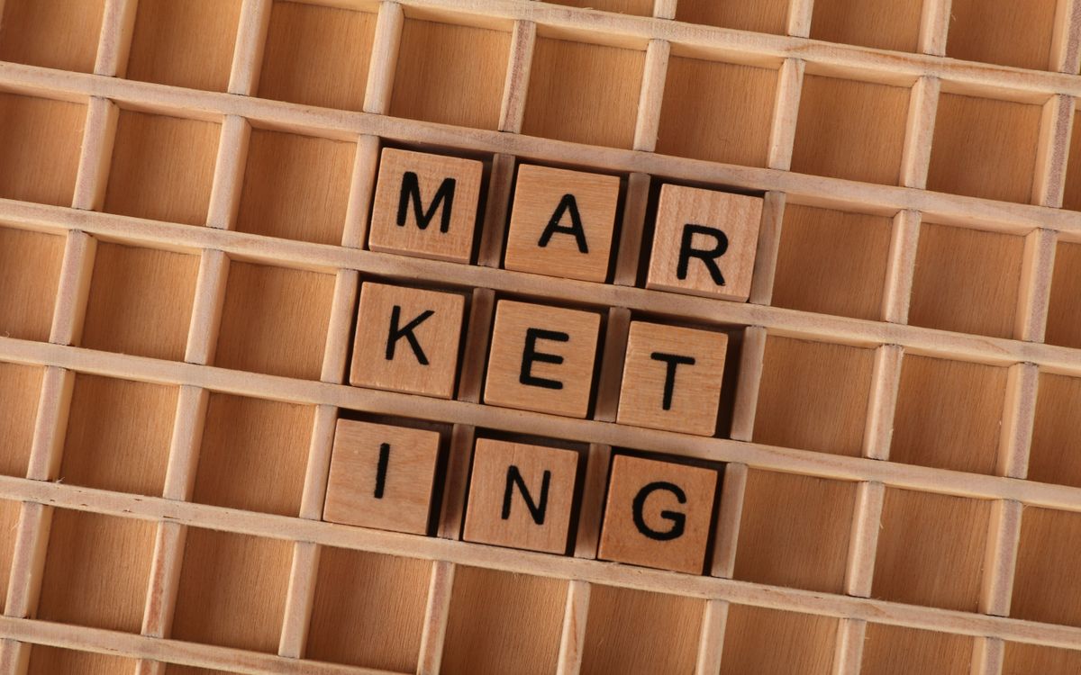 Wooden letter tiles spell out the word marketing on a grid background, showcasing creativity and business concept.