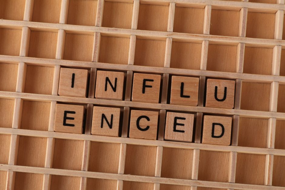 木製の格子状のレイアウト上に並べられた、スクラブルのタイルで「influenced」という単語が綴られている様子をクローズアップした写真。