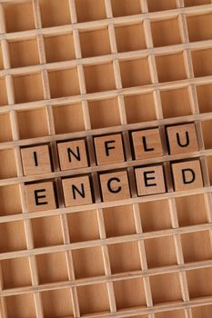 Close-up of wooden Scrabble tiles spelling 'influenced' on a grid.