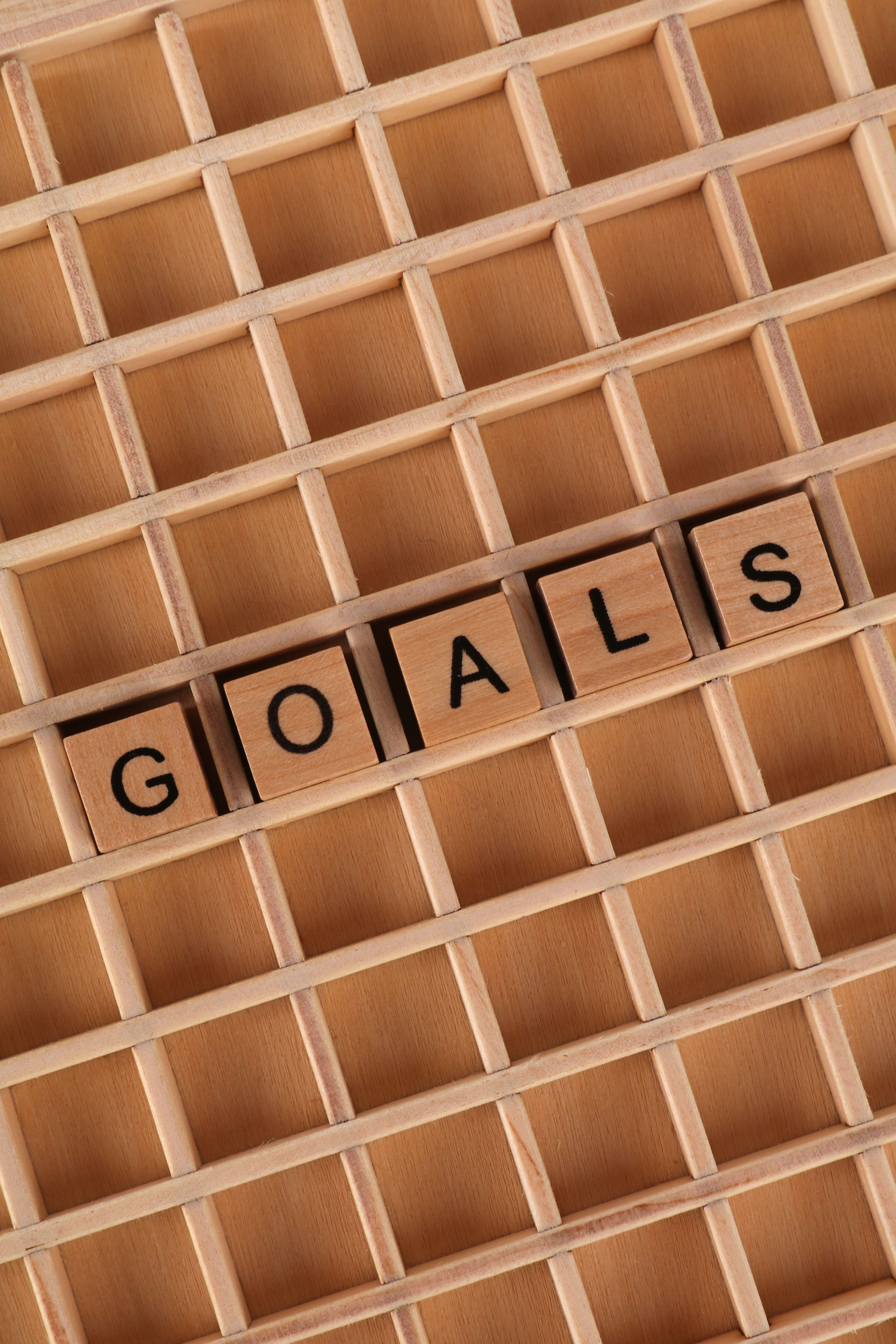 Wooden blocks spelling "goals" on a lattice background, symbolizing achievement.