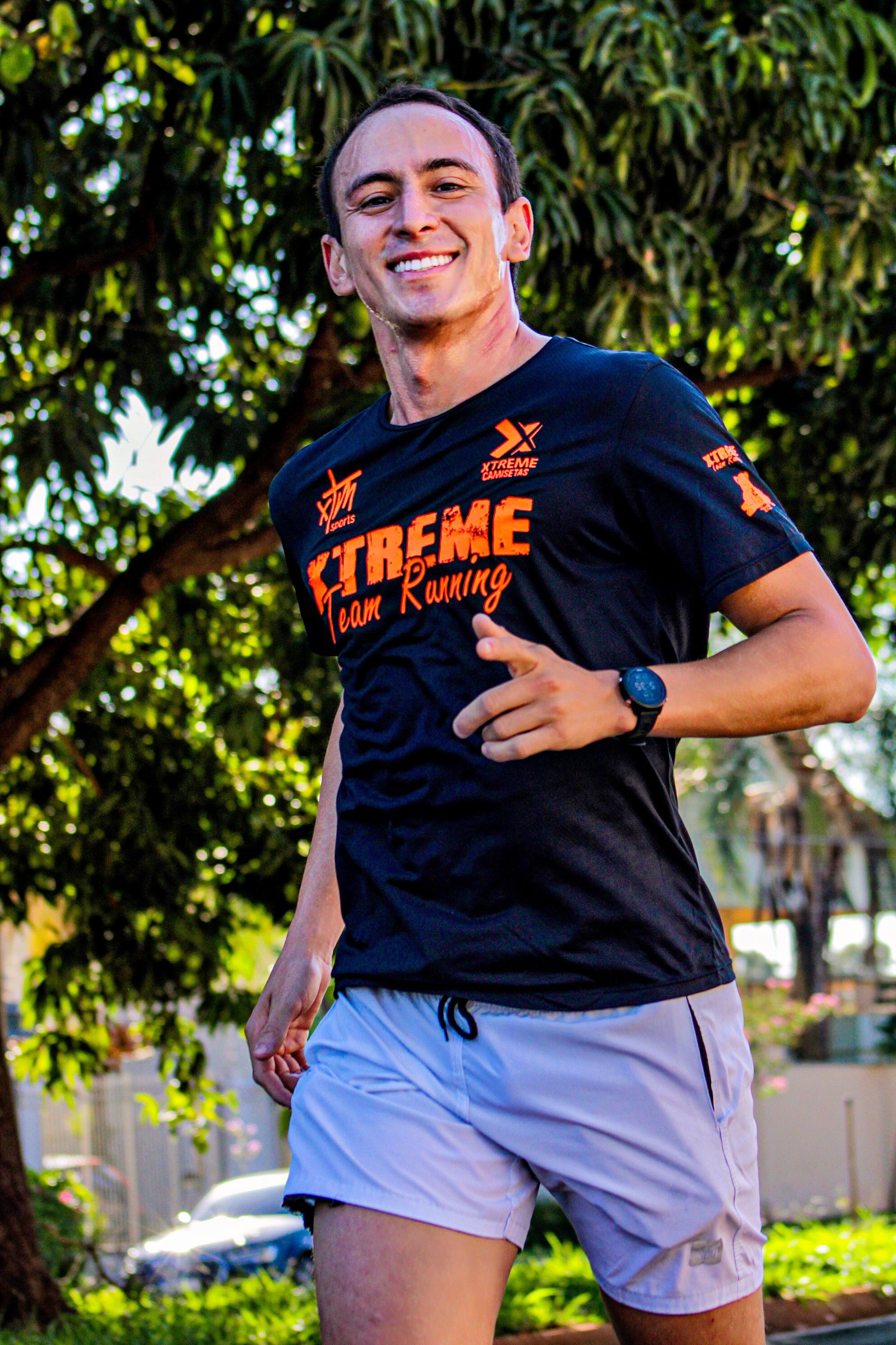 Smiling man jogging in a park, showcasing athletic wear with trees in the background.