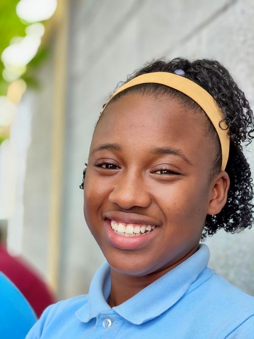 Free Teen girl with a yellow headband smiling warmly outdoors, wearing a blue shirt. Stock Photo