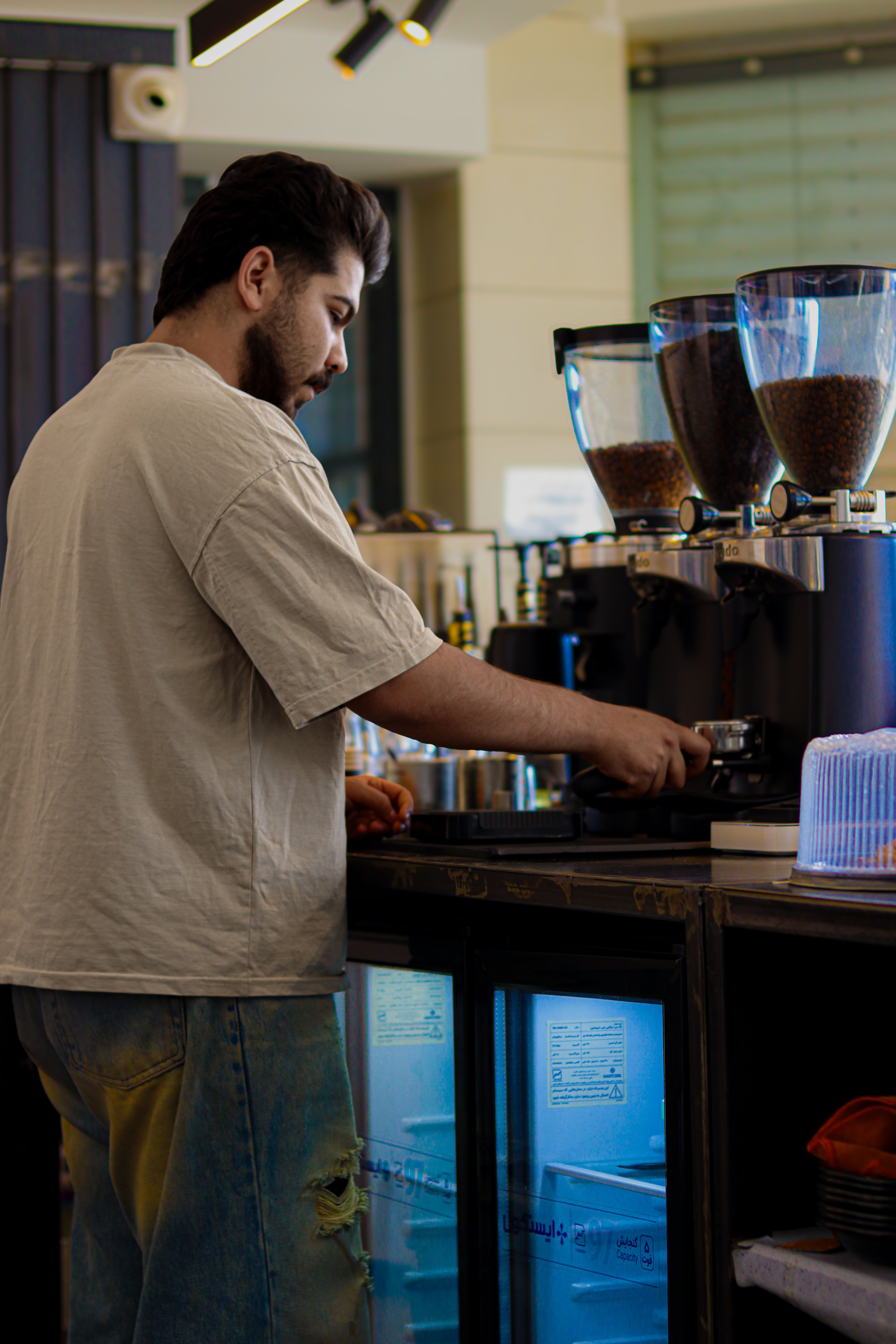 Barista de dos au comptoir, porte-filtre en main devant deux moulins pleins de grains