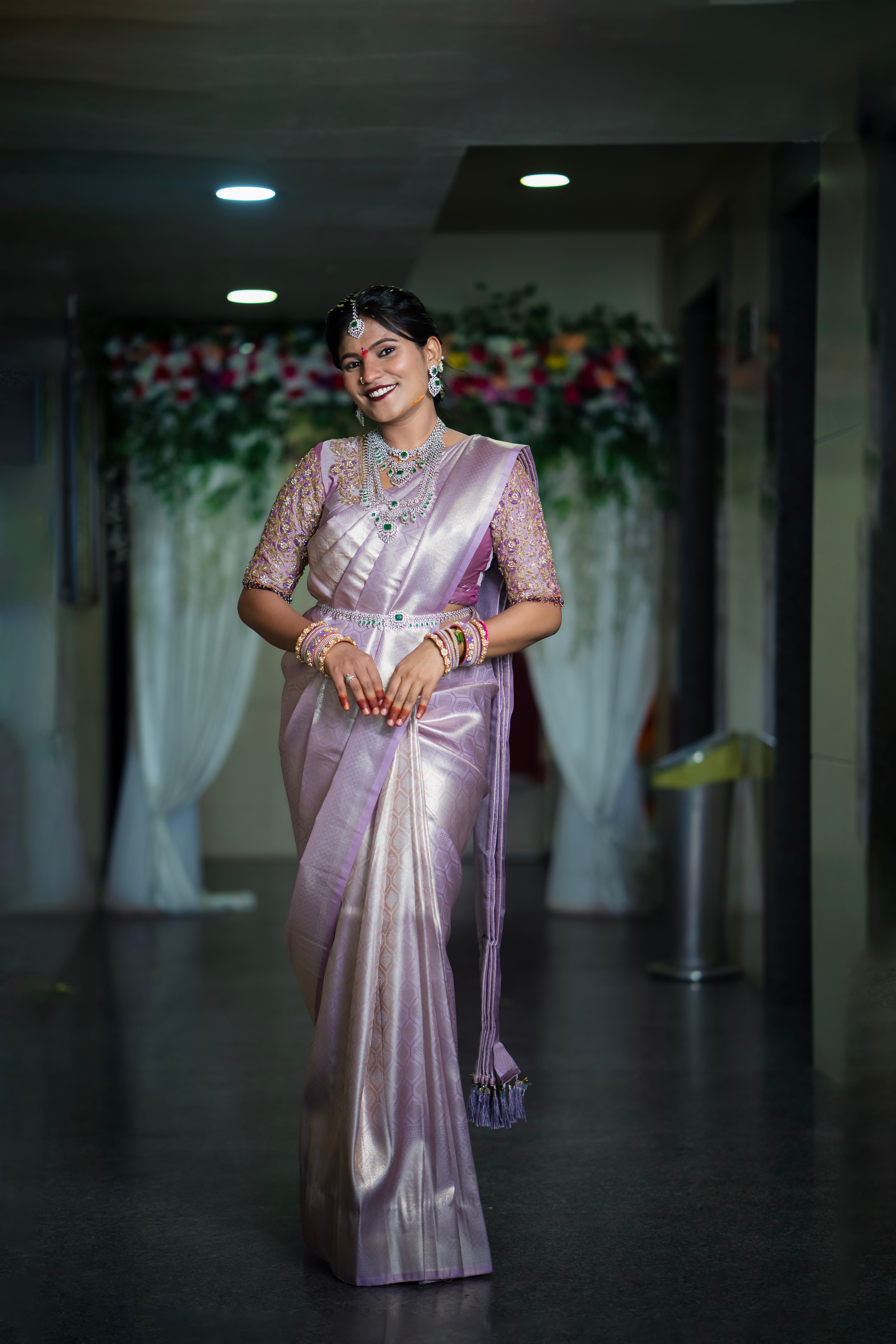 Bride in a lavender saree with floral background at a wedding venue in Hyderabad.