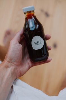 A hand holding a bottle labeled 'loft.7 studio & cafe', filled with iced coffee.