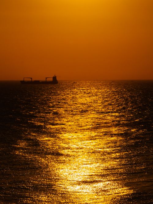 Free Silhouette of a ship at sea during a stunning golden sunset, creating a tranquil and dramatic seascape. Stock Photo