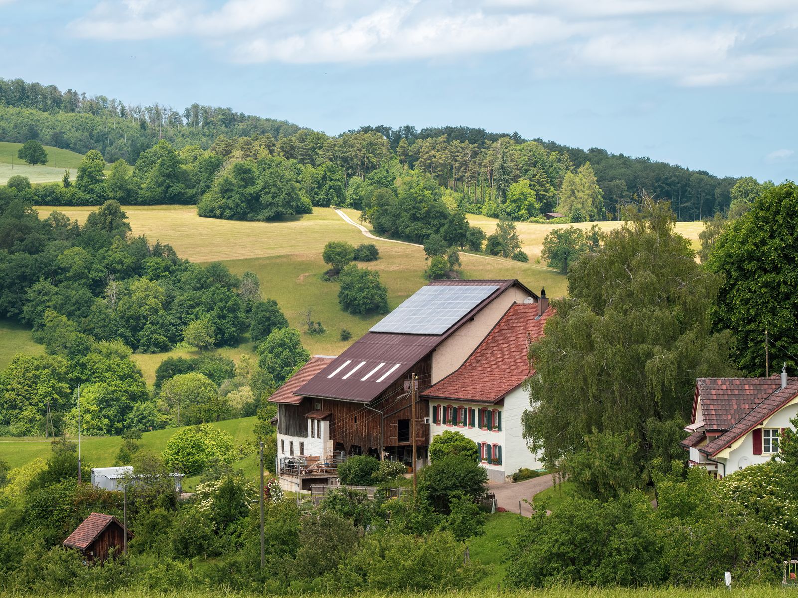 Idyllic farmhouse with solar panels surrounded by lush green fields and forests
