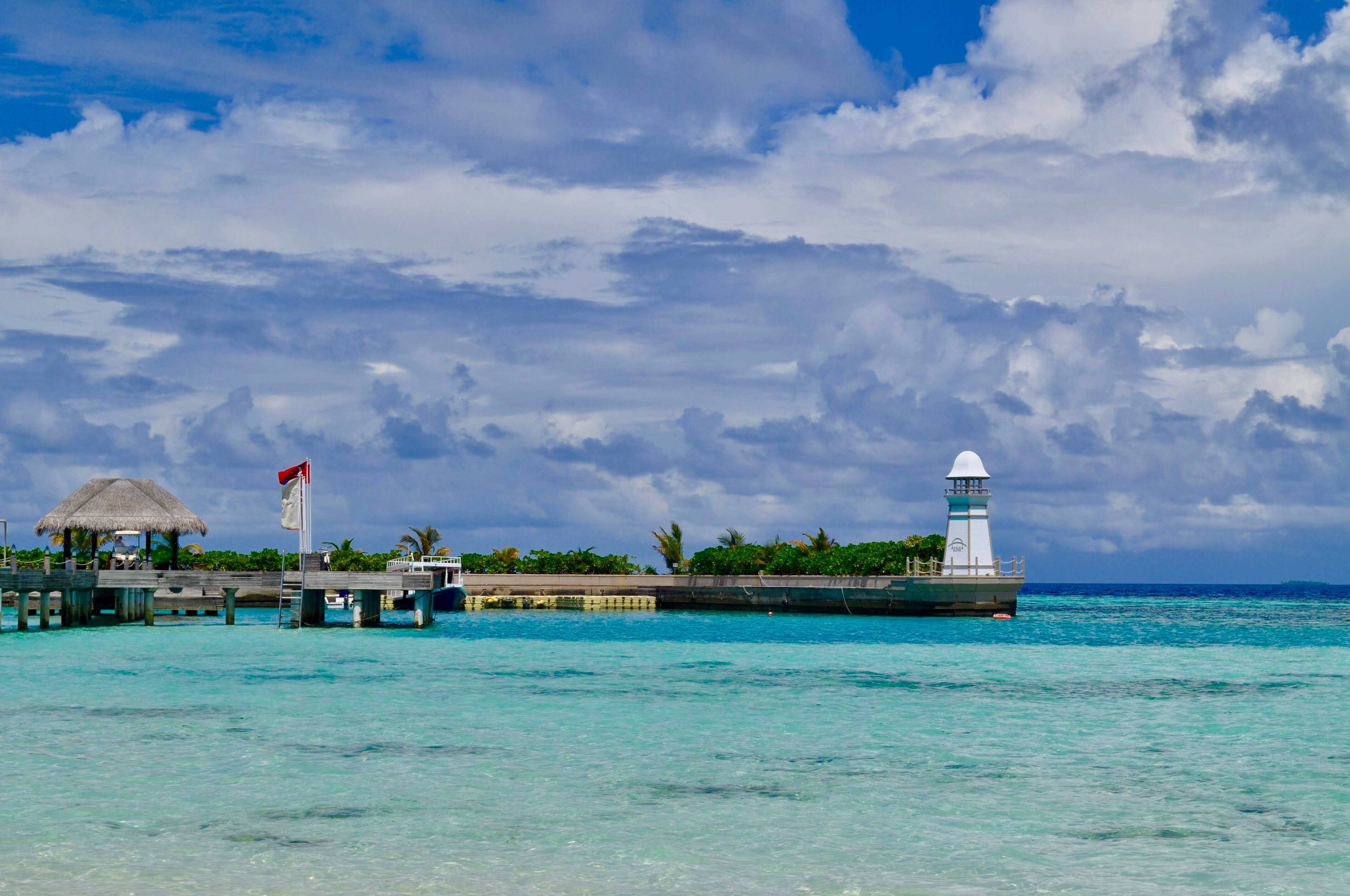 Scenic view of a tropical pier with a lighthouse and azure water under a vibrant sky.
