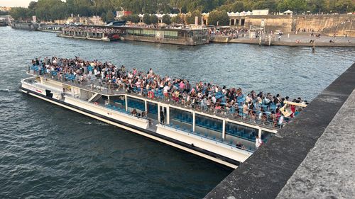 Free A crowded tour boat sails along the Seine River in Paris, with passengers enjoying the vibrant cityscape. Stock Photo