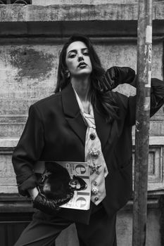 Black and white photo of a fashionable woman posing with a magazine in an urban setting.