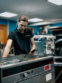 A focused technician inspects equipment in an indoor workshop, holding a tool.