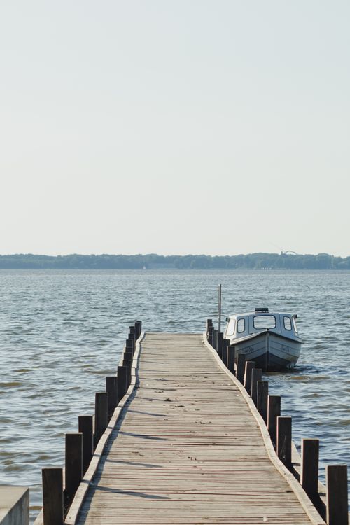 Free Peaceful scene of a wooden dock and boat on Lake Steinhude, Wunstorf, Germany. Perfect for travel inspiration. Stock Photo