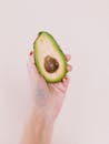 垂直镜头中，手拿着半个新鲜鳄梨，专注于健康和纯素生活方式
