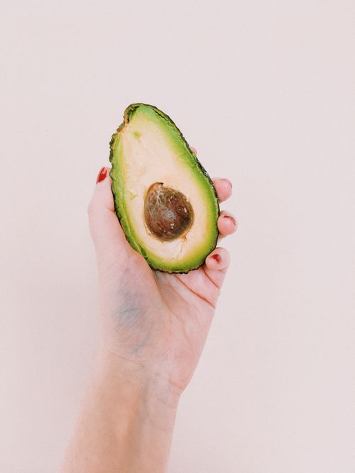 Free Vertical shot of a hand holding half a fresh avocado, focusing on health and vegan lifestyle. Stock Photo
