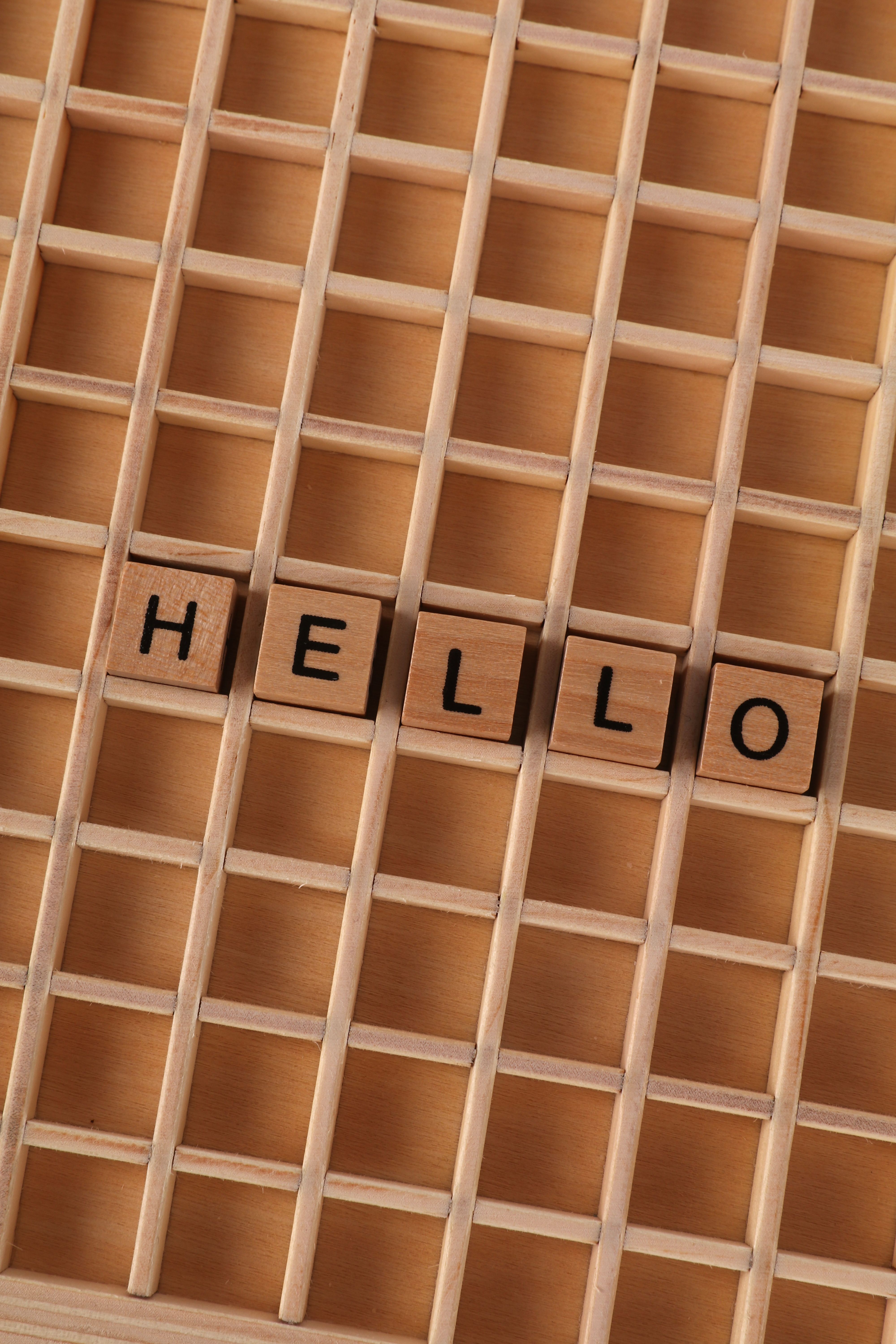 Wooden letter tiles arranged to spell "HELLO" on a wooden grid with natural tones.