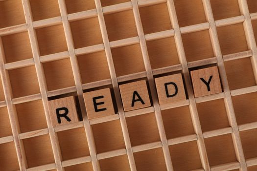 Wooden letter blocks on a grid form the word READY, symbolizing preparation and readiness.