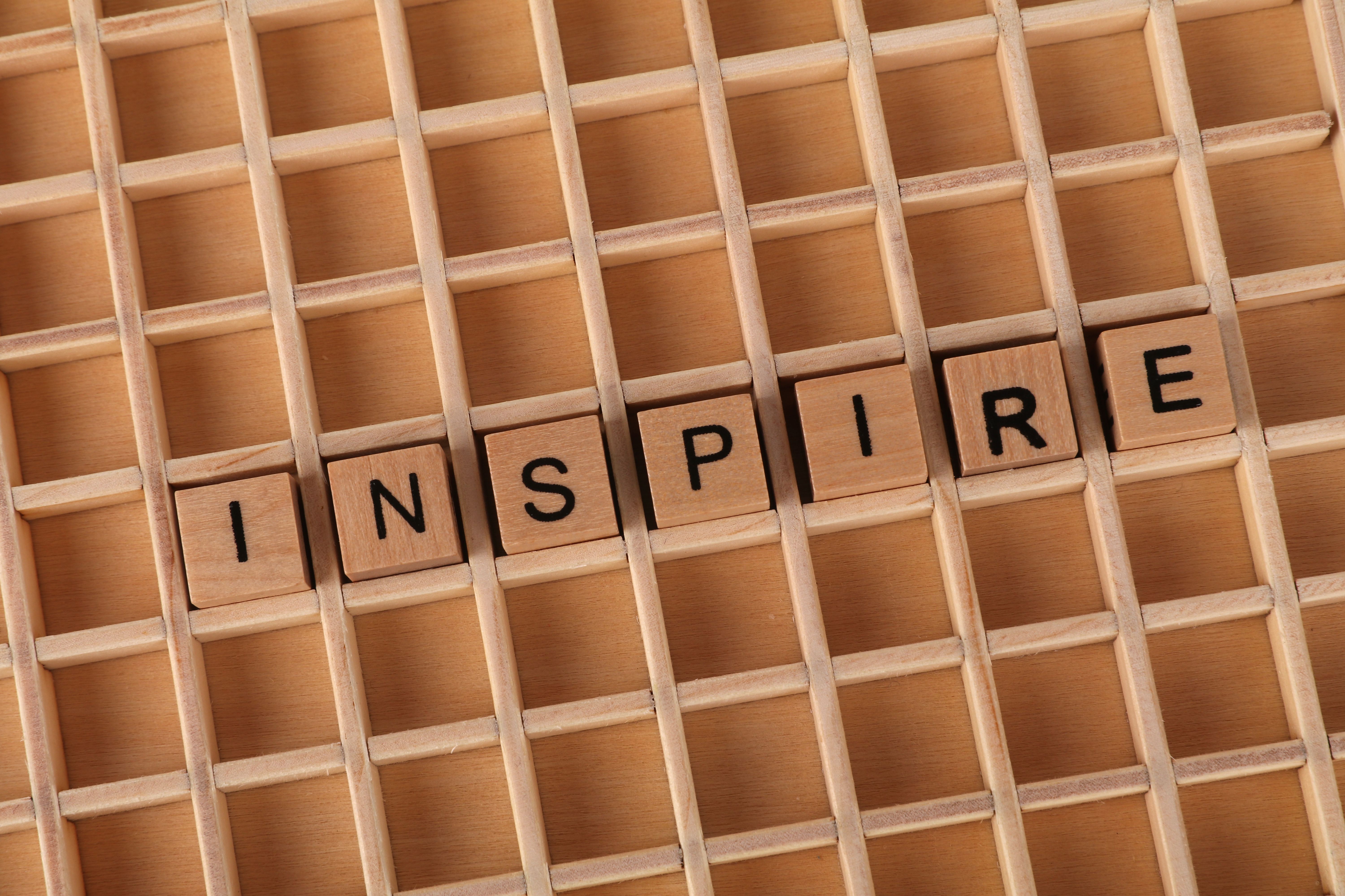 Wooden letter tiles spelling 'INSPIRE' on a grid background symbolize creativity and motivation.