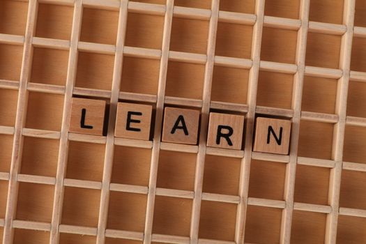 Wooden blocks spelling the word 'LEARN' on a grid-like wooden background. Educational concept.