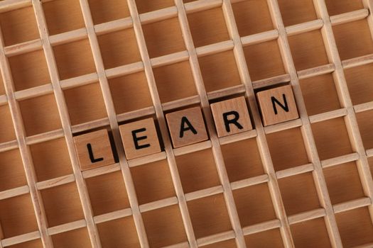 Wooden letter blocks spelling 'Learn' placed on a wooden grid background.