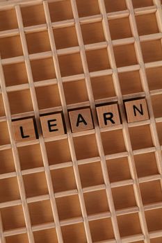 Top view of Scrabble tiles spelling 'Learn' on a wooden grid background.