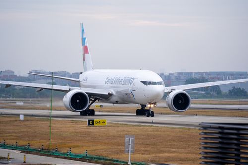 Free A commercial airplane taxis on an airport runway with cityscape in the background. Stock Photo