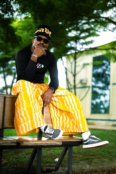 Cool urban fashion shot of a man in trendy yellow pants, sitting outdoors with a confident pose.
