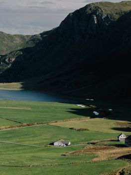 Idyllic Norwegian valley with green fields, mountains, and a serene lake under a cloudy sky.