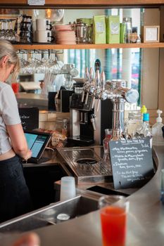 Barista working at cafe counter, preparing a drink near a chalkboard menu.