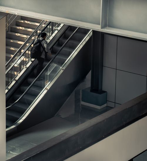 Free A person with a backpack rides an escalator in a modern indoor setting. Stock Photo
