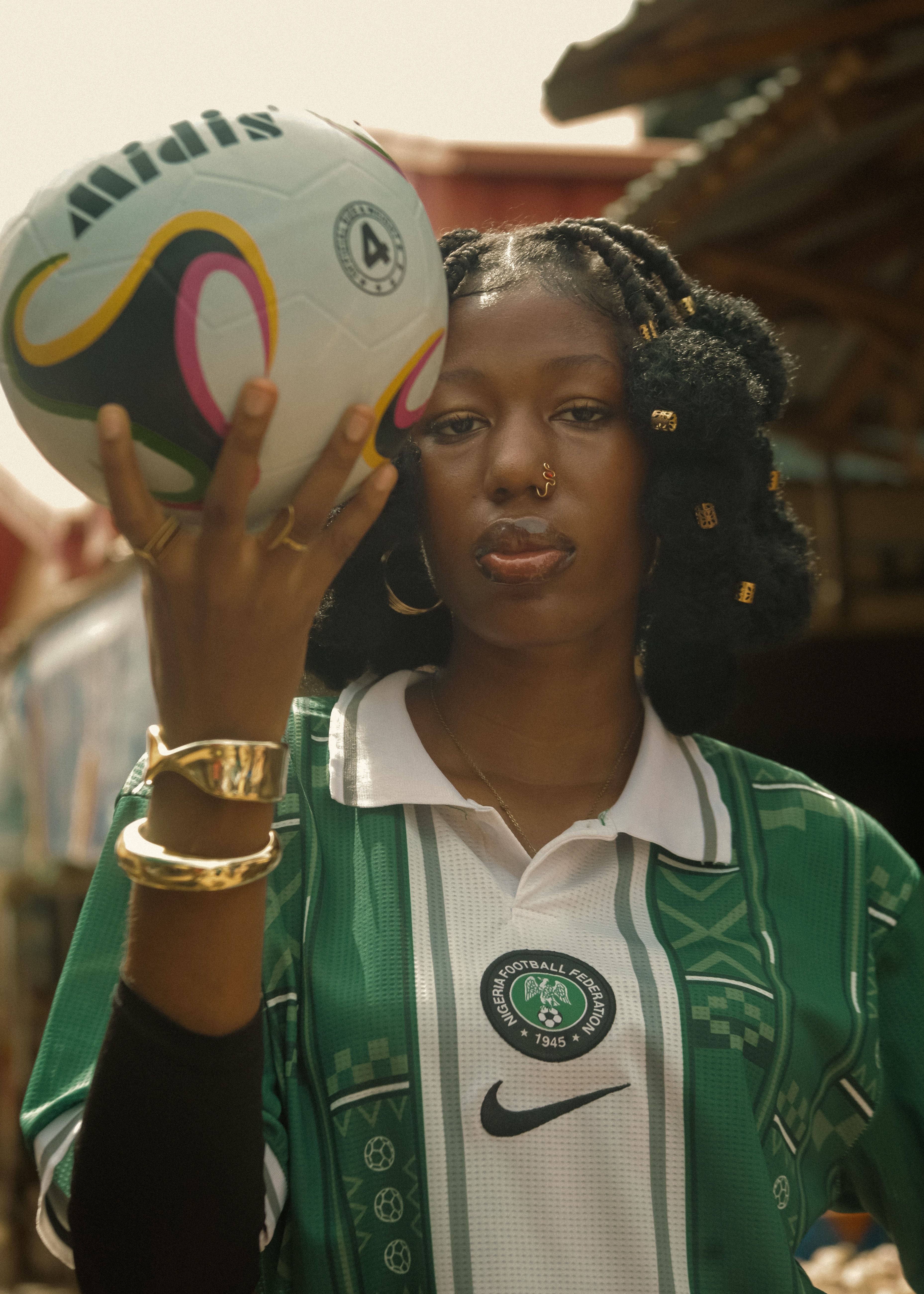 Confident young woman in a green football jersey holding a soccer ball outdoors.