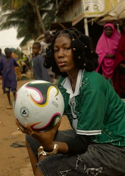A fashionable young woman holds a colorful soccer ball in an outdoor street setting.