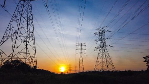 Silhouetted power lines and towers against a striking sunset sky, illustrating energy supply themes.