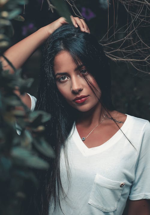 Woman In White V Neck Shirt Standing Beside Green Leaves